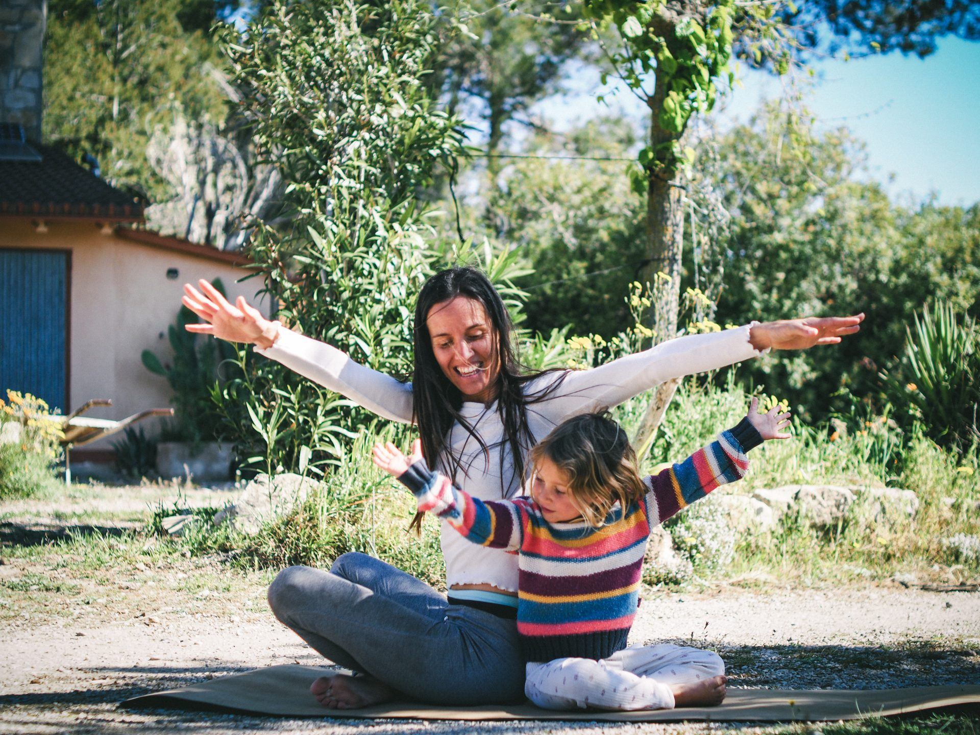 Una adulta y una niña practicando yoga en familia con los brazos abiertos